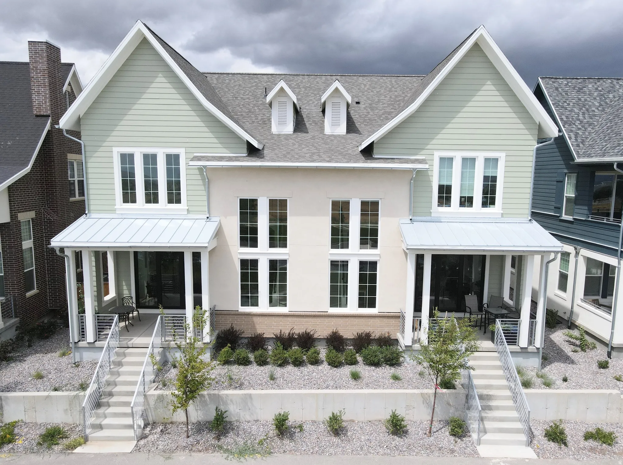 Modern farmhouse duplex featuring symmetrical architectural design with peaked rooflines, dormer windows, and white exterior siding