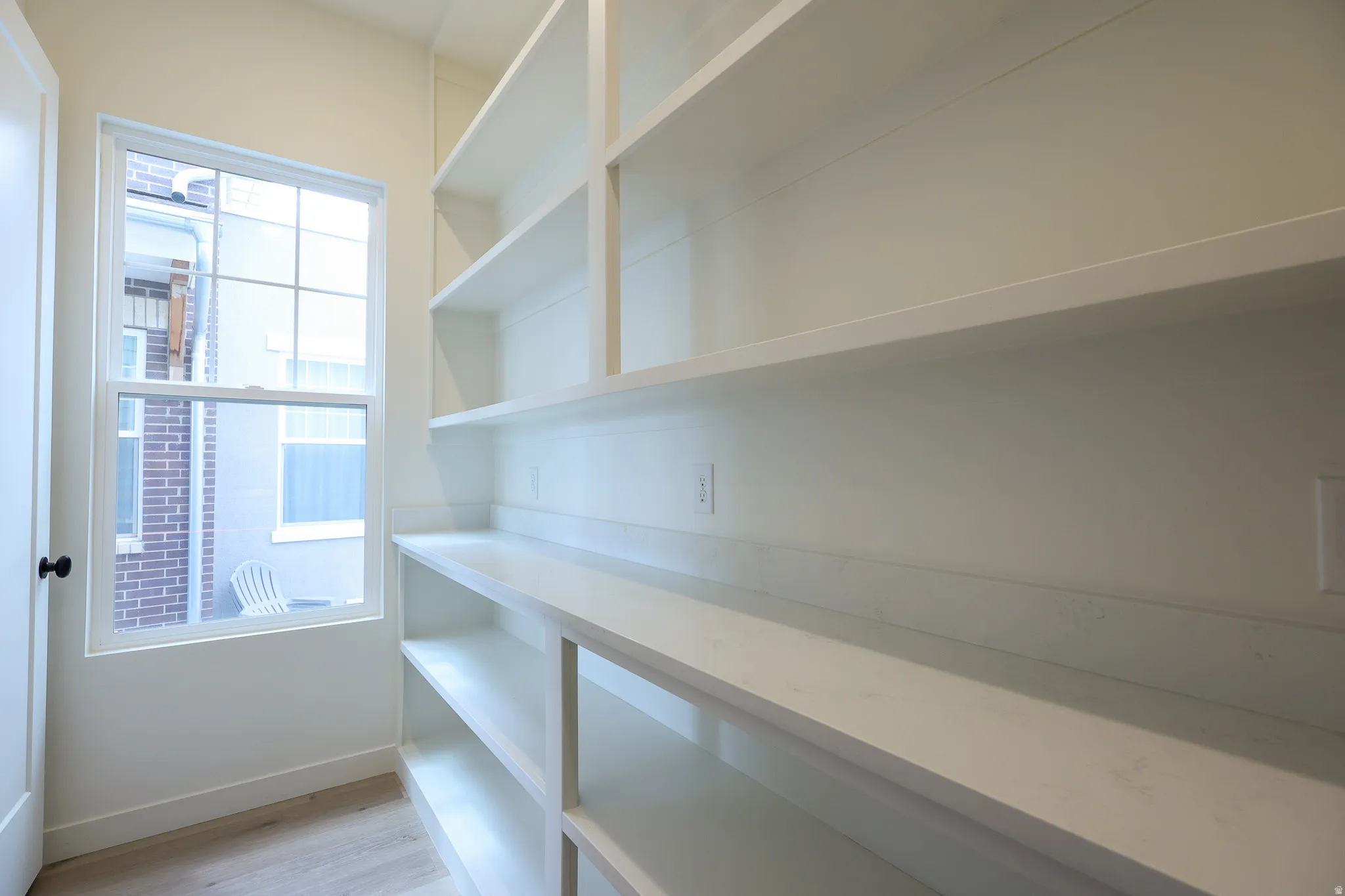 Built-in shelving with multiple storage levels, a window for natural illumination, and light wood-finish flooring
