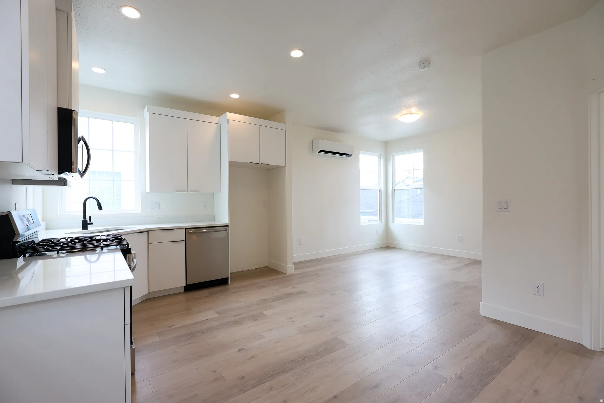 ADU-Kitchen featuring white cabinetry, light countertops, stainless steel dishwasher, gas range, and wood-finish flooring