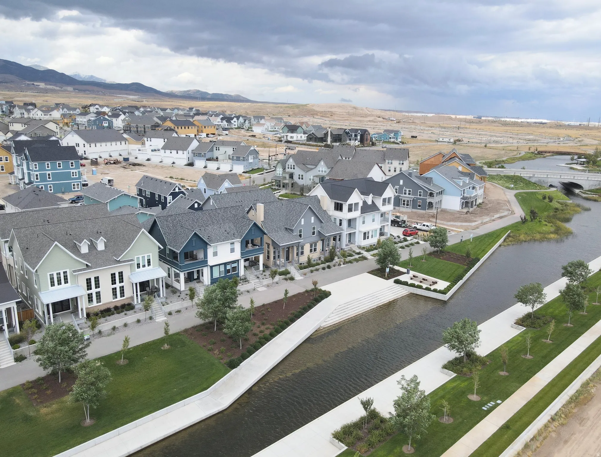 Community with diverse architectural styles, a concrete-lined canal, expansive green spaces, and mountain scenery
