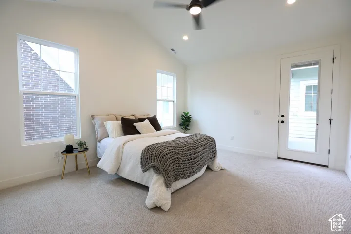 Primary bedroom with Vaulted ceiling, two large windows, white walls, ceiling fan, and a glass-paneled door