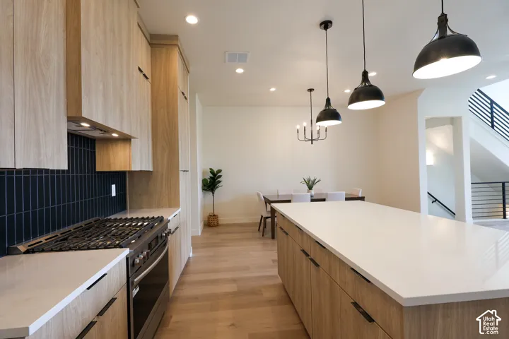 Kitchen featuring wood-finish cabinetry, a large center island with a light-toned countertop, a gas range with a tile backsplash, and recessed lighting
