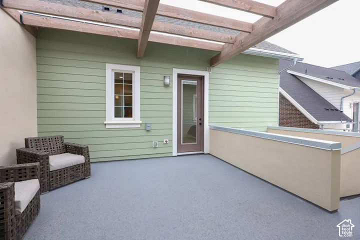 Outdoor terrace featuring a pergola, light green siding, and a neutral-toned privacy wall