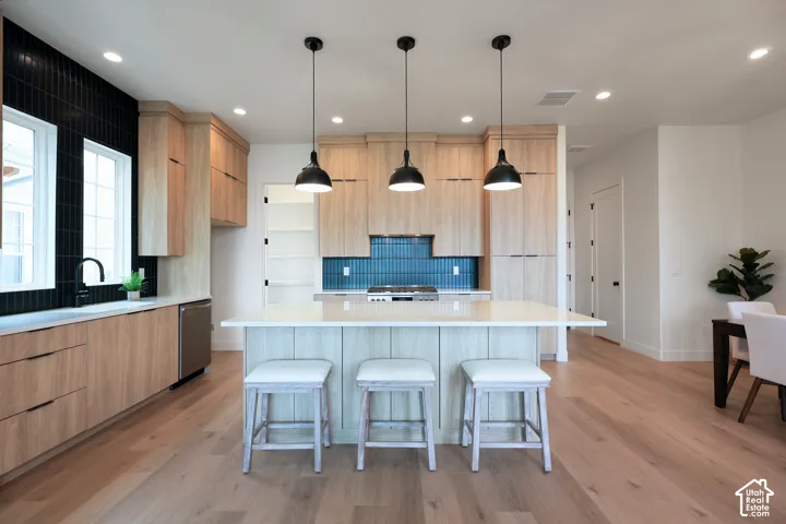 Modern kitchen featuring light wood-finish cabinetry, a large kitchen island with counter seating, stainless steel appliances, and a tiled backsplash