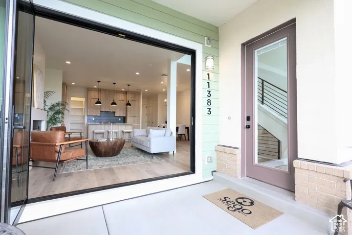 Expansive glass bi-fold doors open to an interior with wood-finish flooring, a contemporary kitchen with a dark tile backsplash, and light wood cabinetry