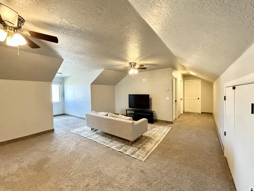Expansive carpeted room featuring vaulted ceilings, recessed window, and ceiling fans