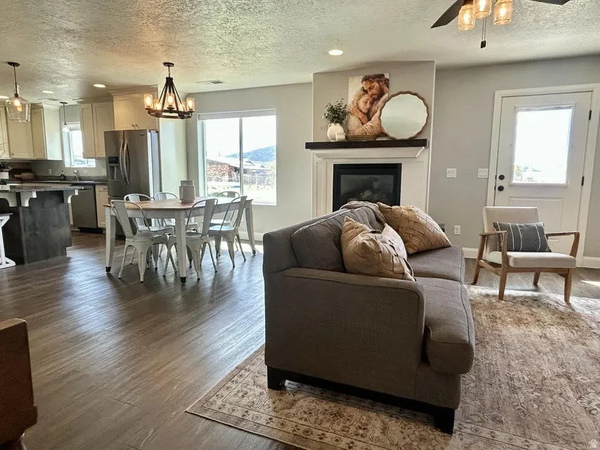 Open concept living area featuring wood-finish flooring, a built-in fireplace with mantel, and a ceiling fan with integrated lighting