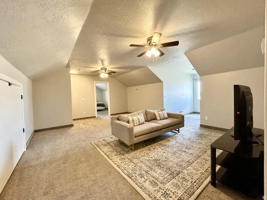 Carpeted living area with vaulted ceilings, two ceiling fans, and a window