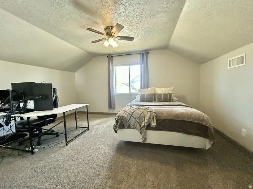 Vaulted ceiling with a ceiling fan, carpeted flooring, and a window with curtains