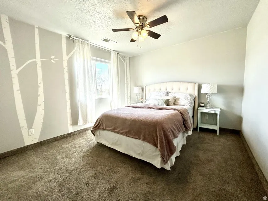 Carpeted bedroom with a ceiling fan light fixture, a window with sheer drapes, and an upholstered headboard