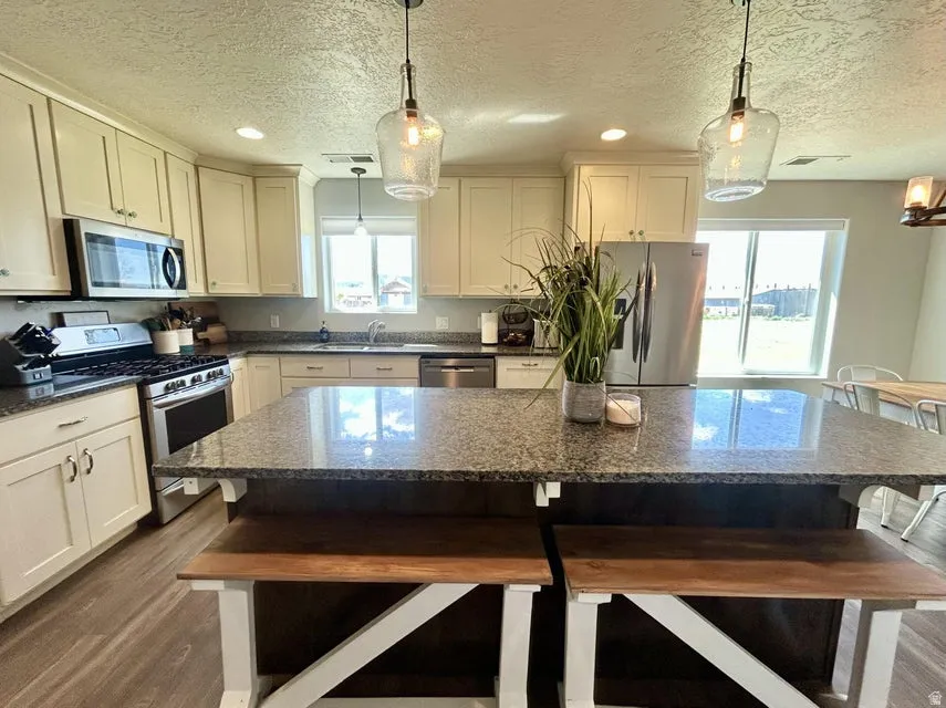 Kitchen featuring granite countertops, stainless steel appliances, wood-finish flooring, white cabinetry, and a center island with seating