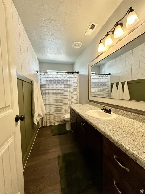 Bathroom featuring a long single-sink vanity with a speckled countertop, rich wood-finish cabinetry, and a large mirror