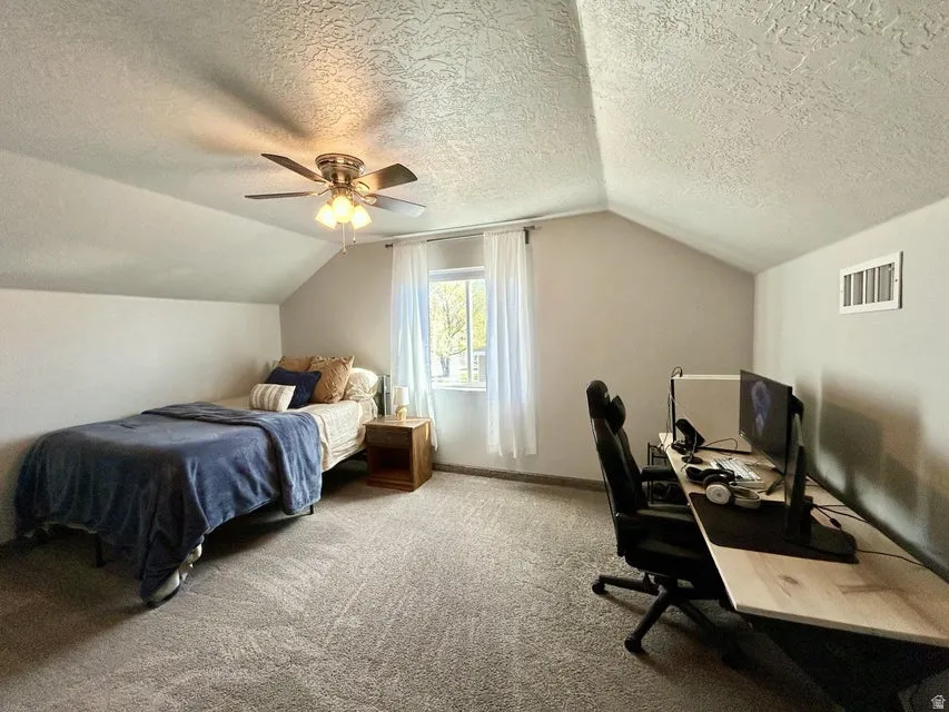 Sloped ceilings, window with natural light, ceiling fan, and grey carpeting