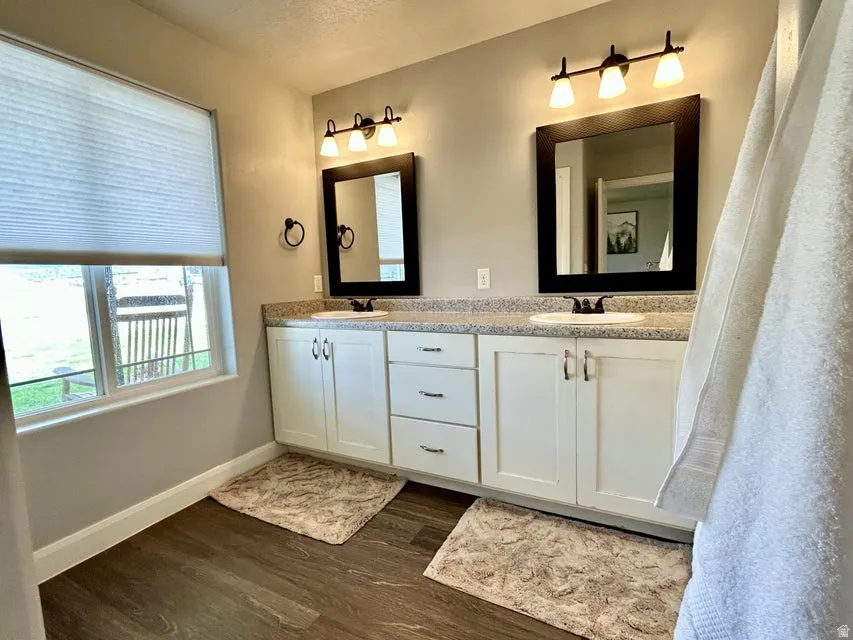 Dual vanity with white cabinetry and chrome hardware, speckled countertop, and wood-finish flooring