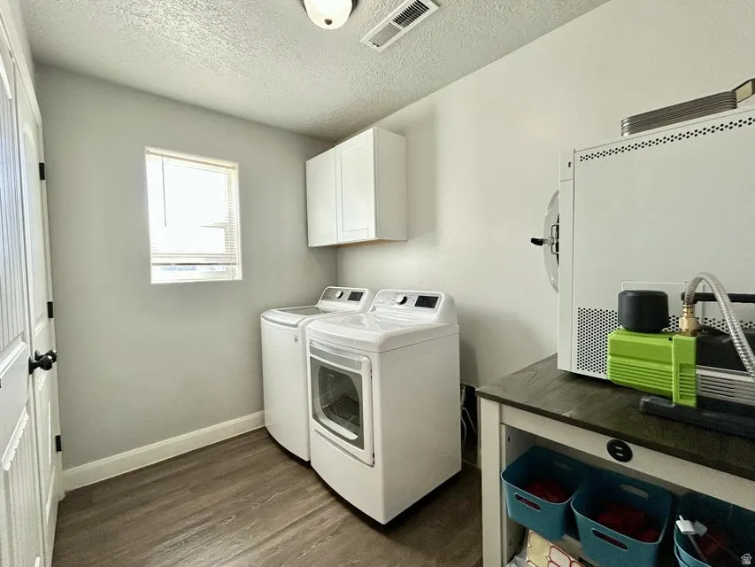 Laundry area featuring wood-finish flooring, a window with blinds, and white upper cabinetry