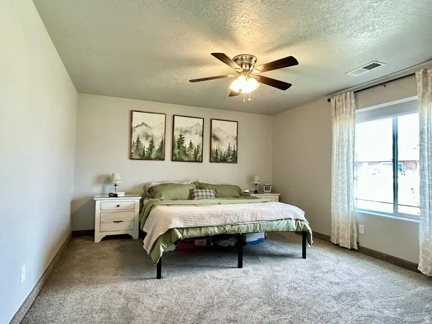 Spacious room featuring carpeting, a ceiling fan with light fixture, and a large window