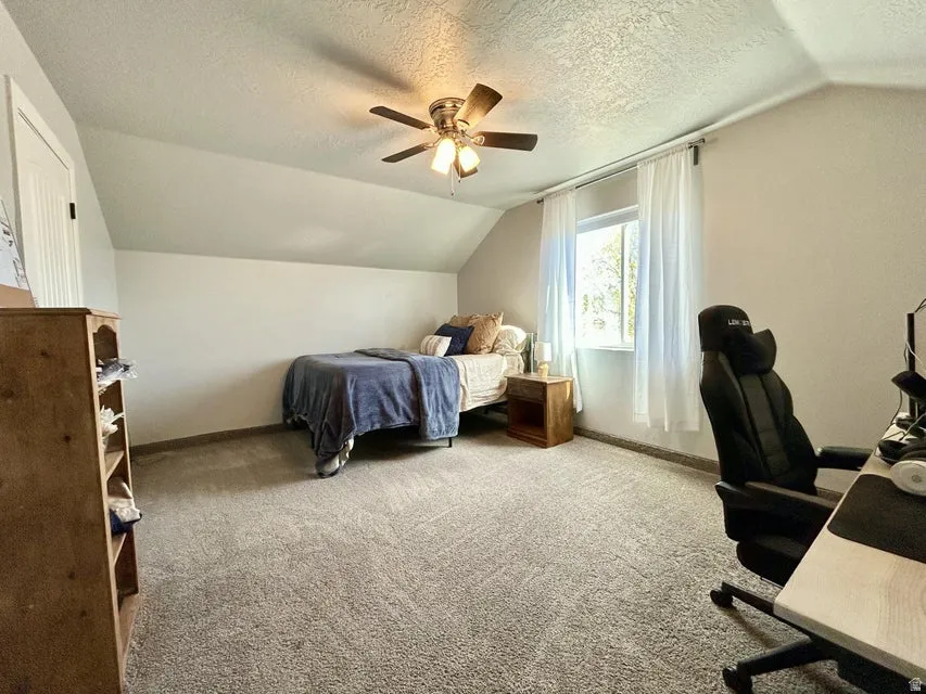 Sloped ceilings with a ceiling fan, light gray carpeting, and a single window with white trim