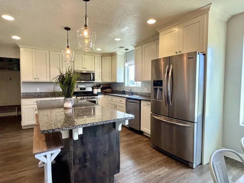 Open-concept kitchen featuring wood-finish flooring, white cabinetry, granite countertops, and stainless steel appliances