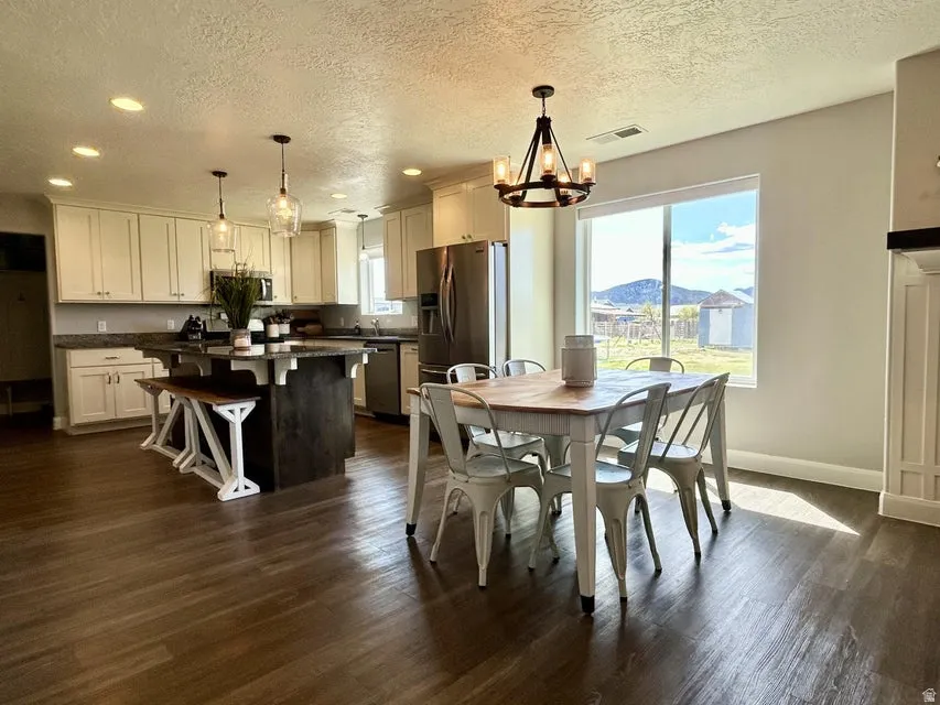 Open-concept kitchen and dining area featuring wood-finish flooring, white cabinetry, a kitchen island with built-in seating, and a large window