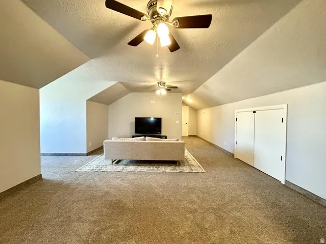 Expansive carpeted room featuring vaulted ceilings, recessed lighting, and multiple ceiling fans