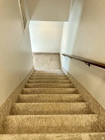 Carpeted staircase with a wood-finish handrail and light-toned wall finishes