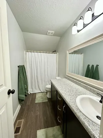 Full bathroom featuring wood-finish flooring, a white shower curtain, and a vanity with a white sink and dark cabinetry