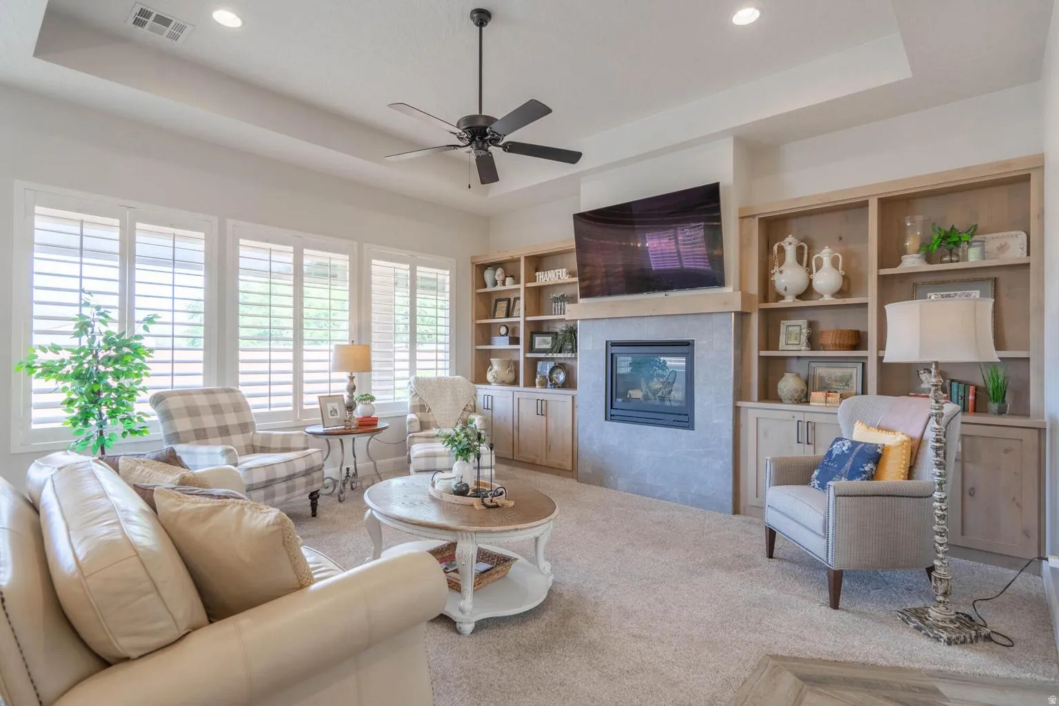 Recessed lighting, ceiling fan, built-in shelving, integrated fireplace, and multiple windows with plantation shutters