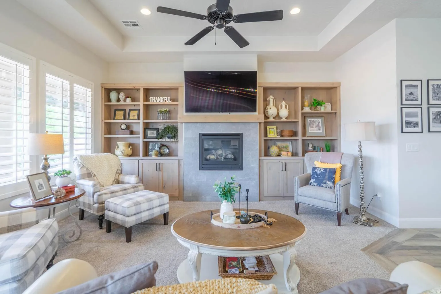 Recessed lighting, ceiling fan, fireplace with a stone surround and wood mantle, built-in shelving, and tray ceiling