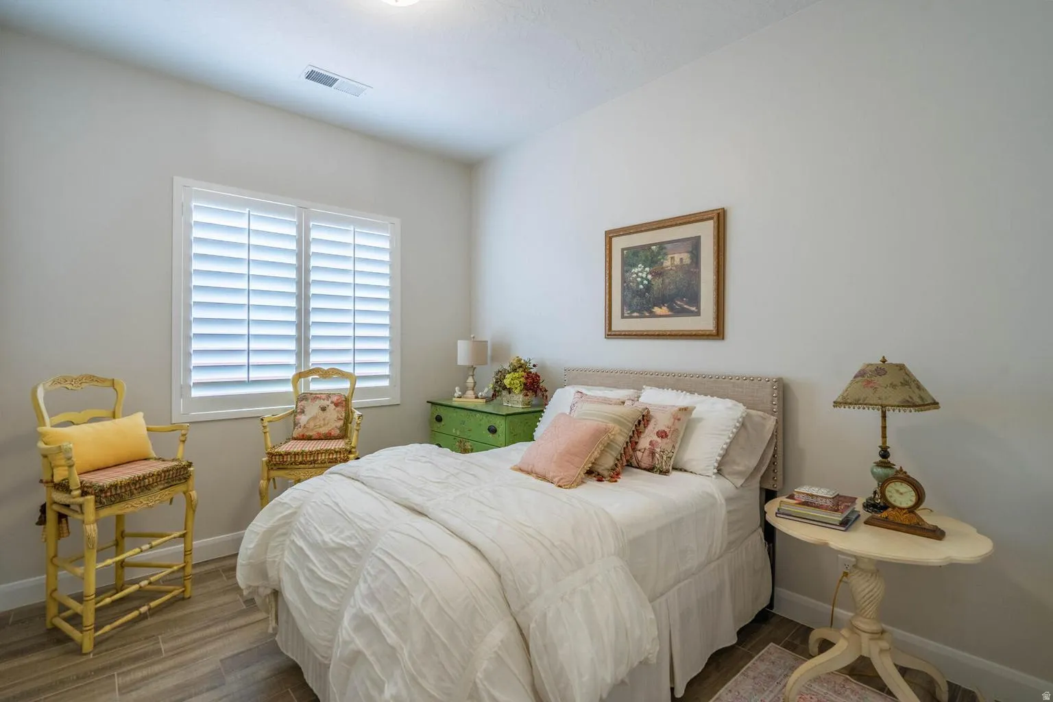 Window featuring white plantation shutters, light gray wall paint, wood-finish flooring, and a neutral upholstered headboard