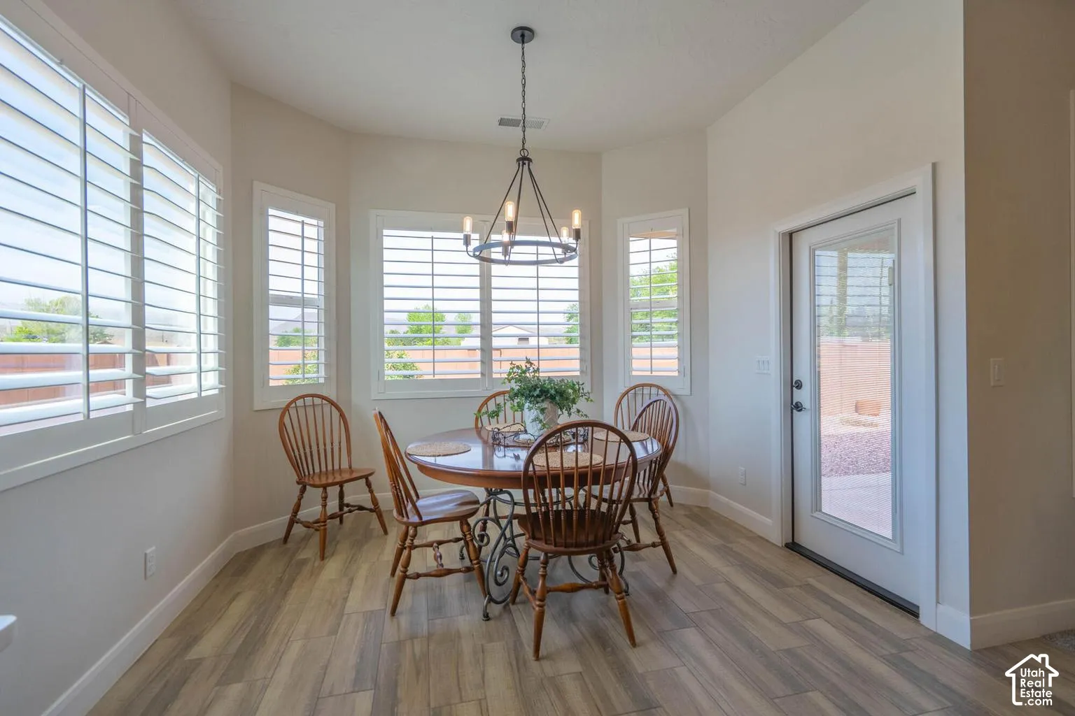 Bay window configuration with multiple windows, plantation shutters, wood-finish flooring, and a glass-paneled exterior door