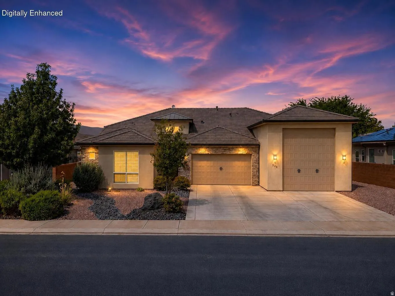 Stucco exterior with stone accents, two attached garages, covered entry, front landscape with mature plantings, and concrete driveway