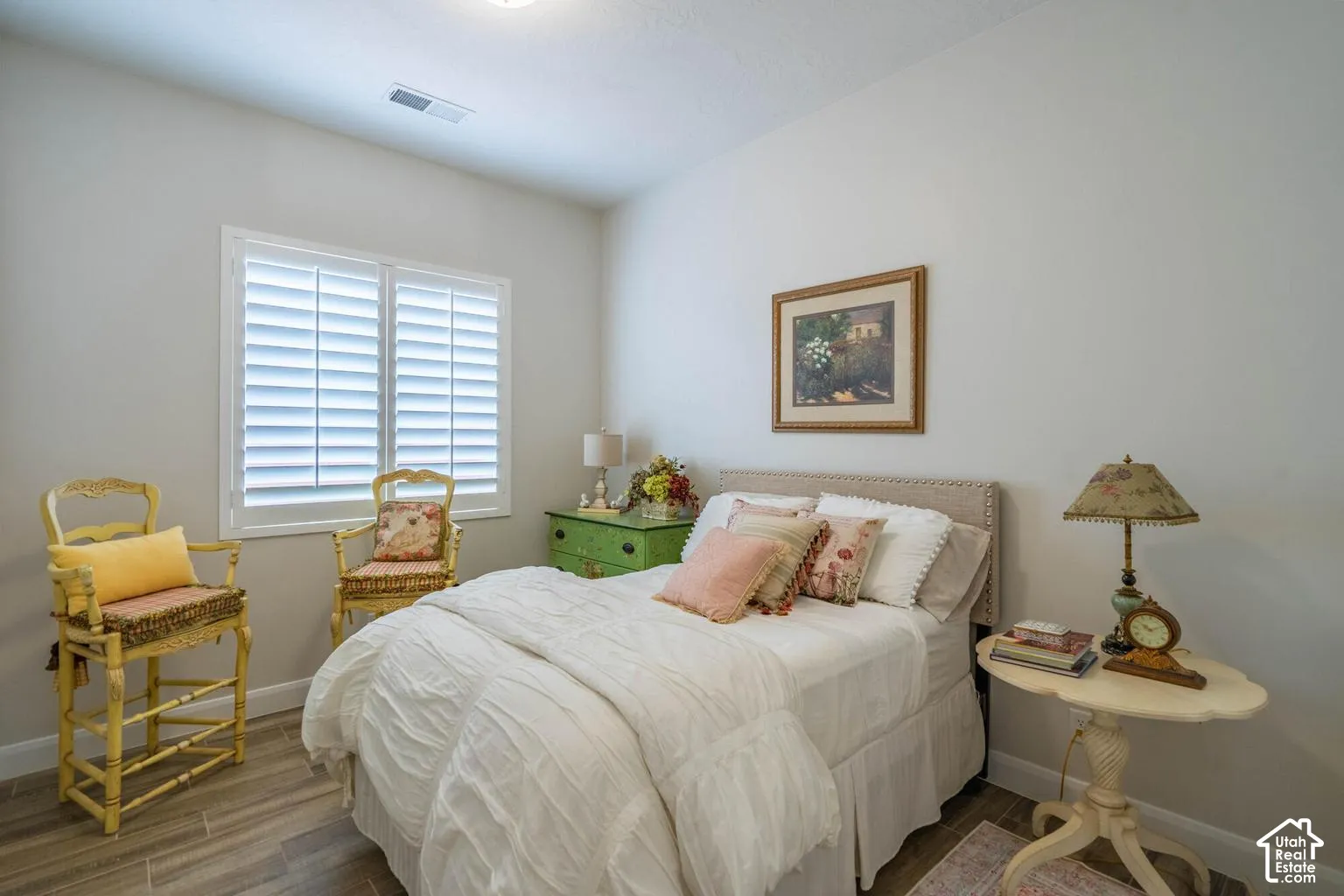 Window featuring white plantation shutters, light gray wall paint, wood-finish flooring, and a neutral upholstered headboard