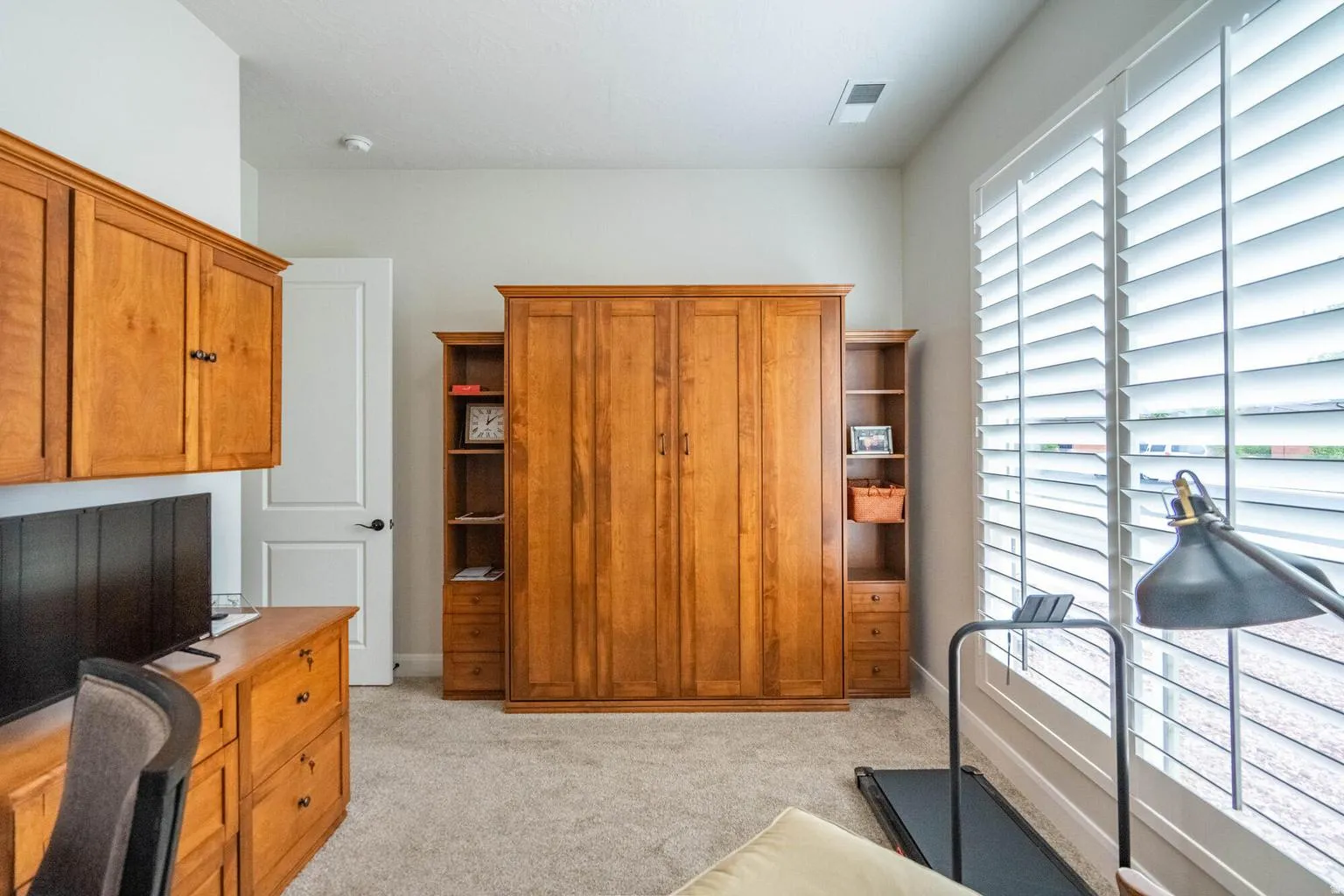 Built-in wood-finish cabinetry, wall-to-wall carpeting, wood-finish shelving, and expansive window with white plantation shutters