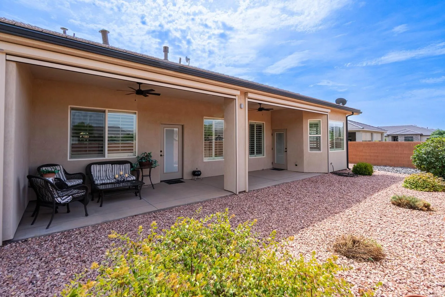 Covered patio with concrete flooring, multiple windows featuring plantation shutters, and ceiling fans