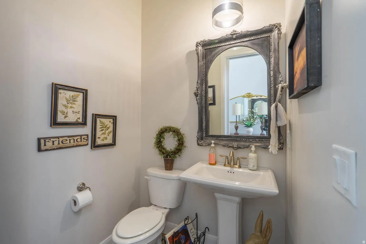 Pedestal sink with brass-finish faucet, ornate framed mirror, and a wall-mounted light fixture
