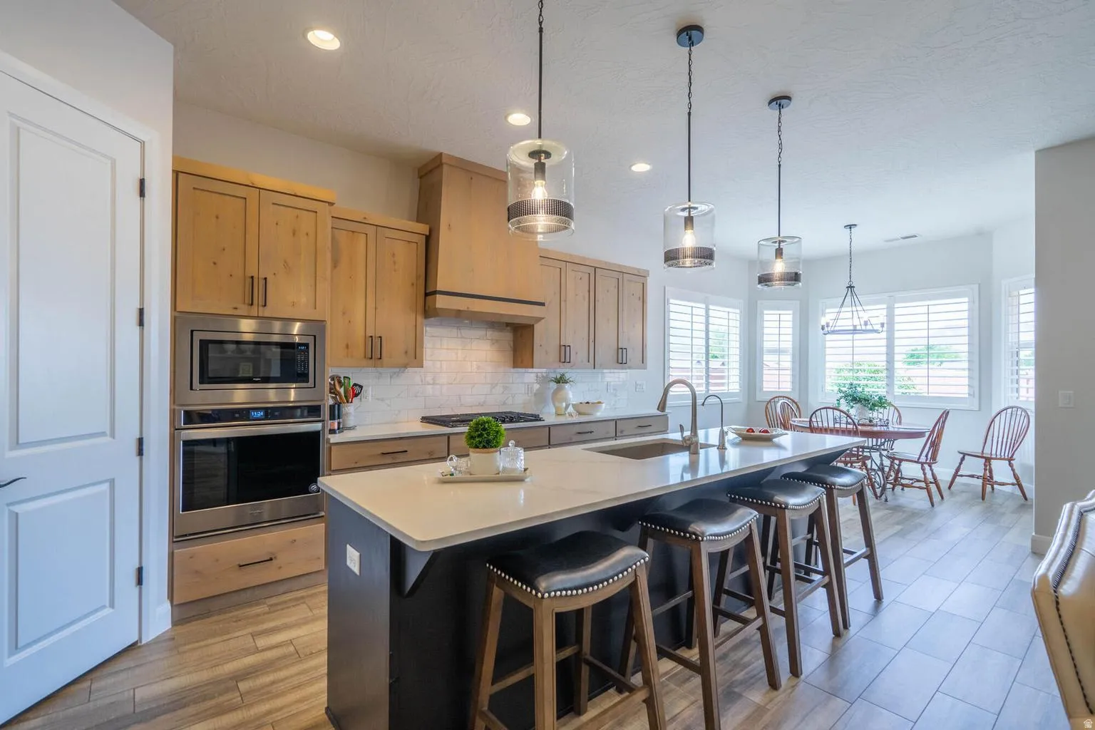 Kitchen featuring wood-finish flooring, light wood cabinetry, white subway tile backsplash, stainless steel appliances, and an island with a light-toned countertop