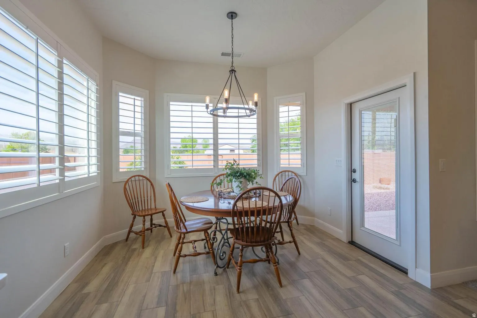 Bay window configuration with multiple windows, plantation shutters, wood-finish flooring, and a glass-paneled exterior door