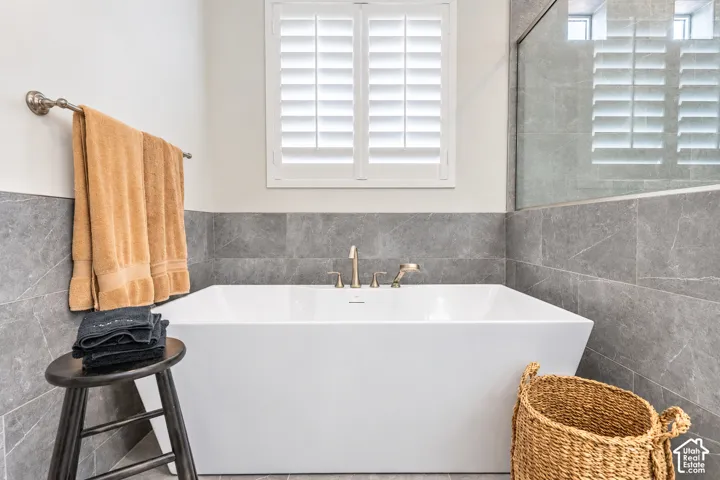 Freestanding soaking tub with brushed brass fixtures, complemented by full-height wall tiling and an adjacent glass-enclosed shower