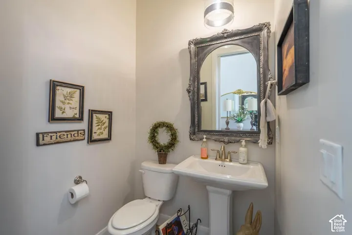 Pedestal sink with brass-finish faucet, ornate framed mirror, and a wall-mounted light fixture