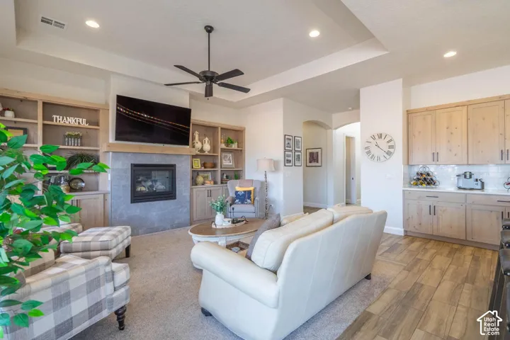 Recessed lighting, ceiling fan, built-in shelving, fireplace with stone surround, and wood-finish flooring