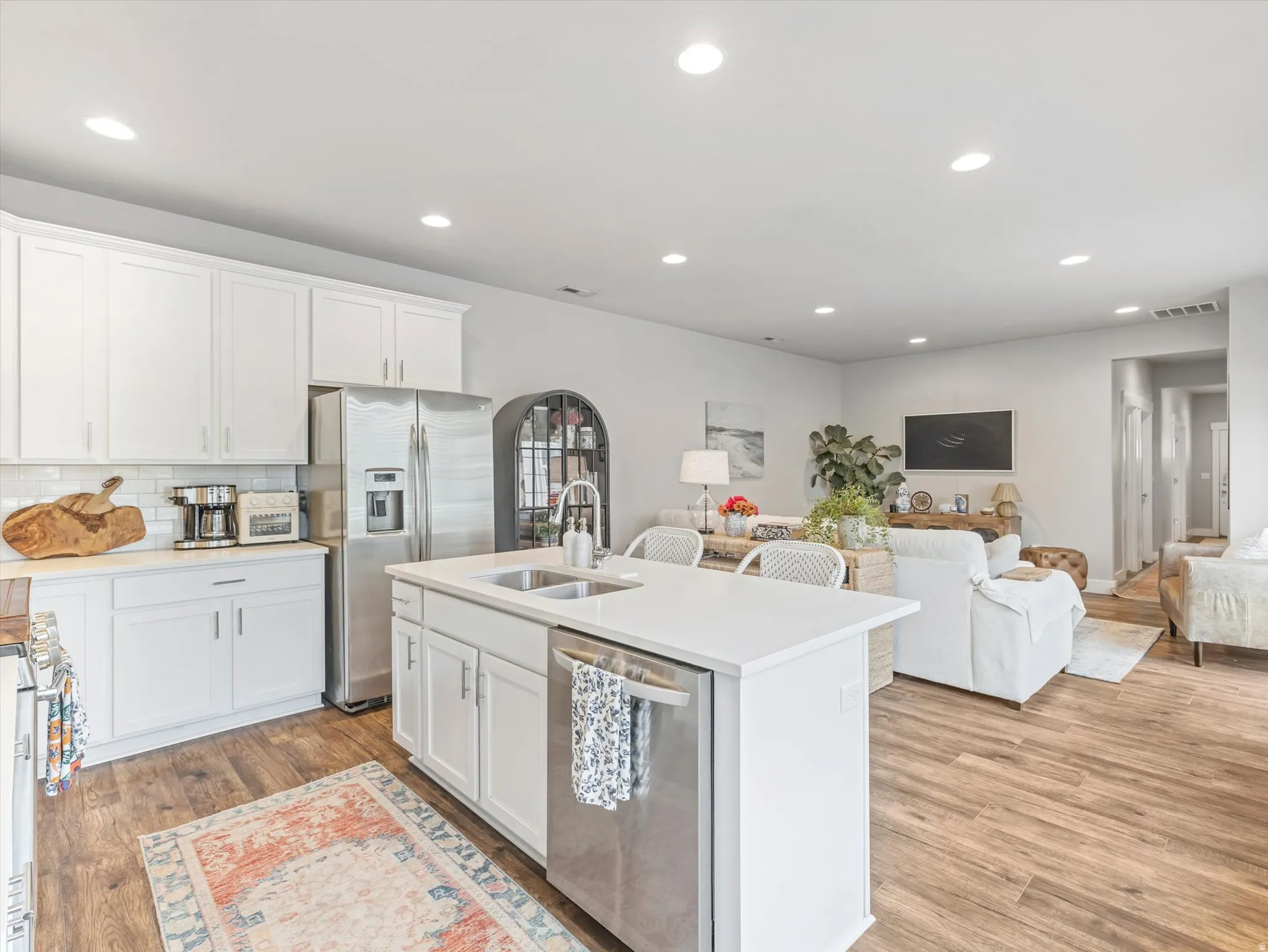 Kitchen featuring white cabinetry, subway tile backsplash, stainless steel appliances, and a central island with an integrated sink