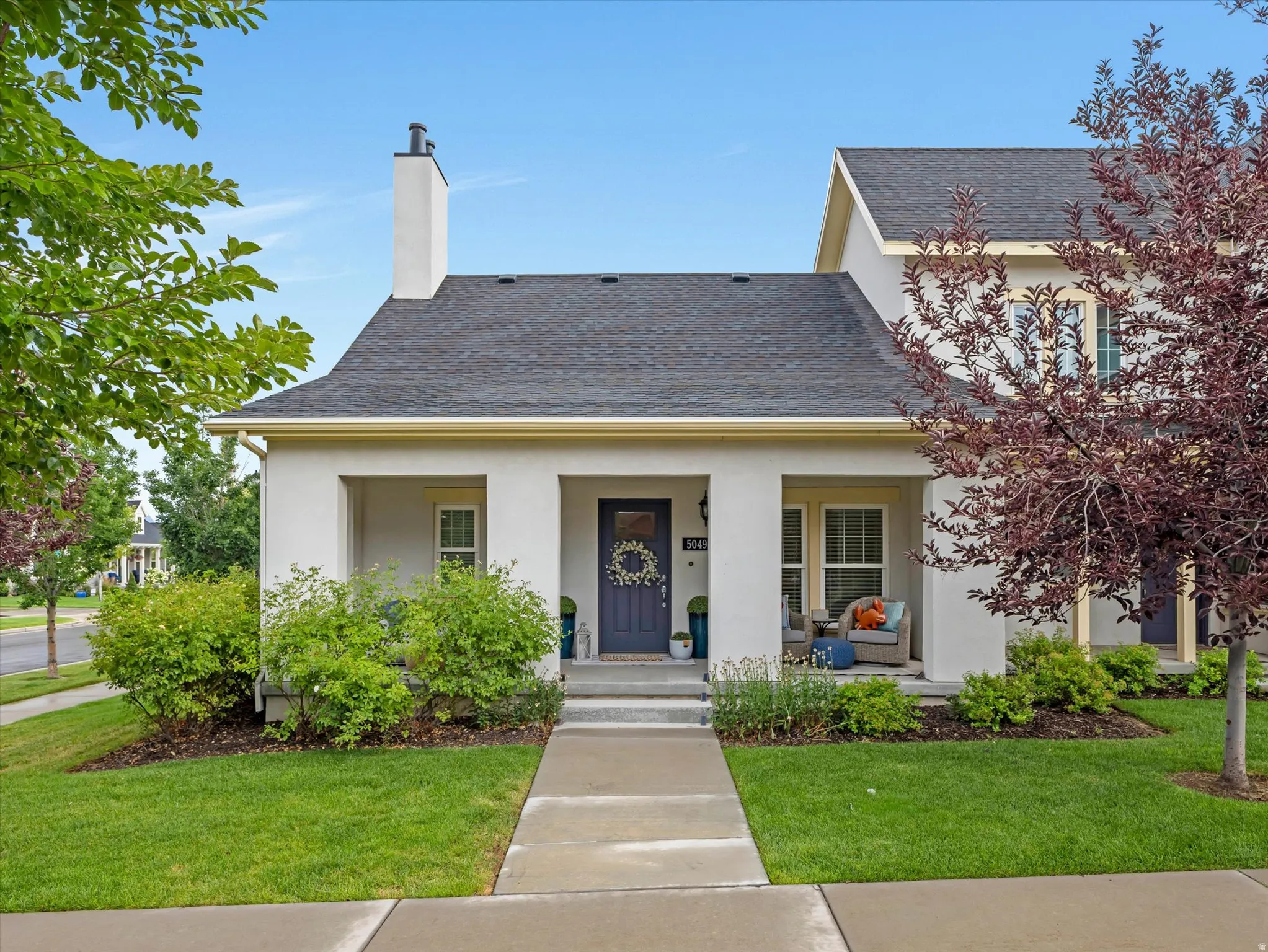 Stucco exterior with dark shingle roofing, featuring a covered front porch and a prominent chimney