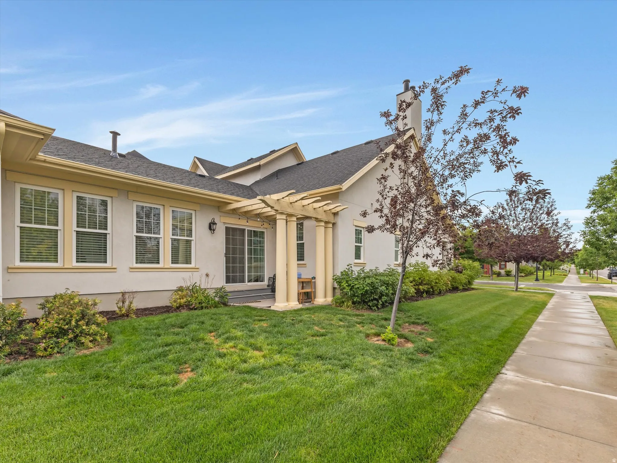 Expansive lawn area with a sidewalk, mature trees, and a stucco exterior