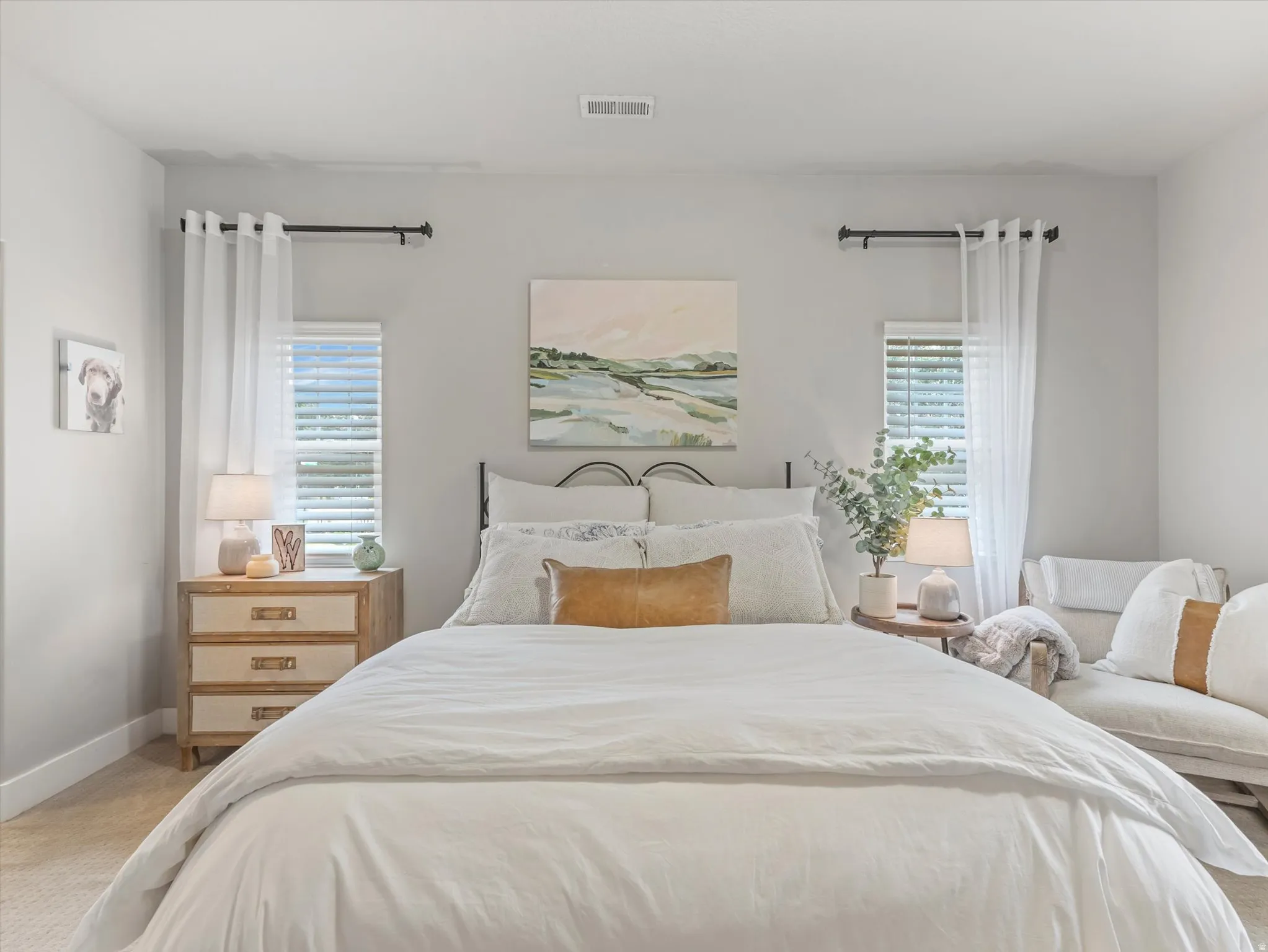Two windows with blinds and sheer curtains, light gray wall paint, and carpeted flooring