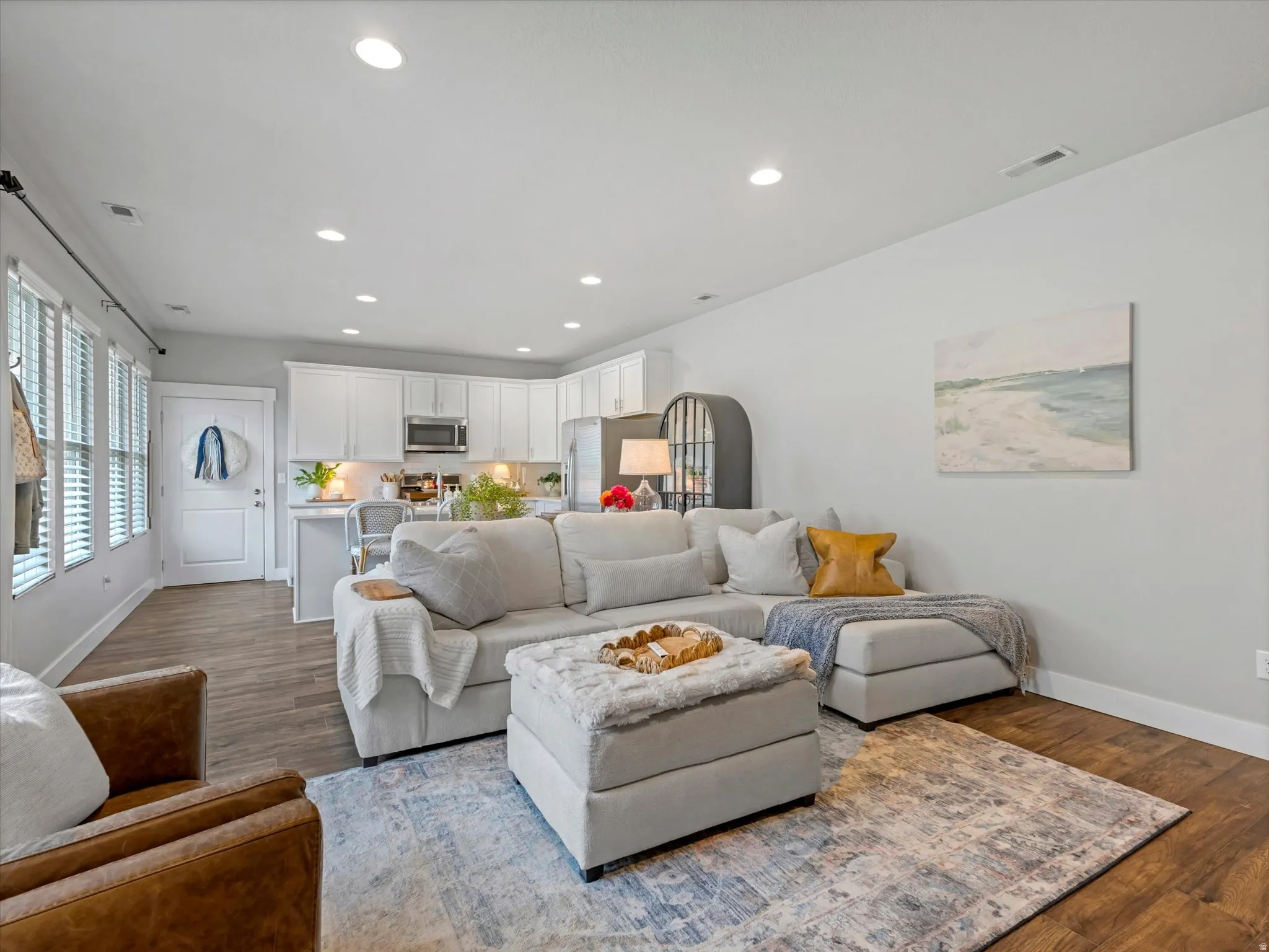 Recessed lighting throughout, wood-finish flooring, white kitchen cabinetry, stainless steel appliances, and a breakfast bar