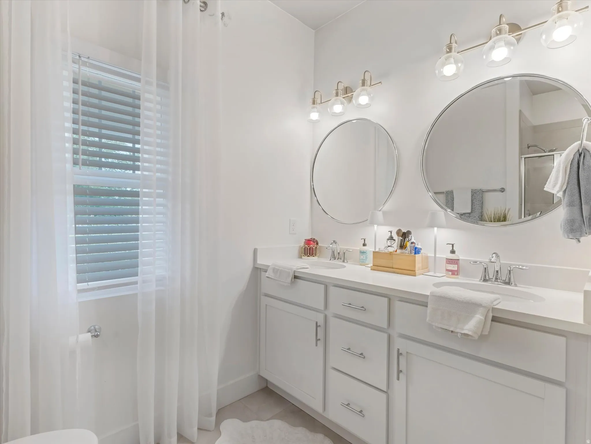 Dual sink vanity with white cabinetry, polished chrome fixtures, and two circular mirrors