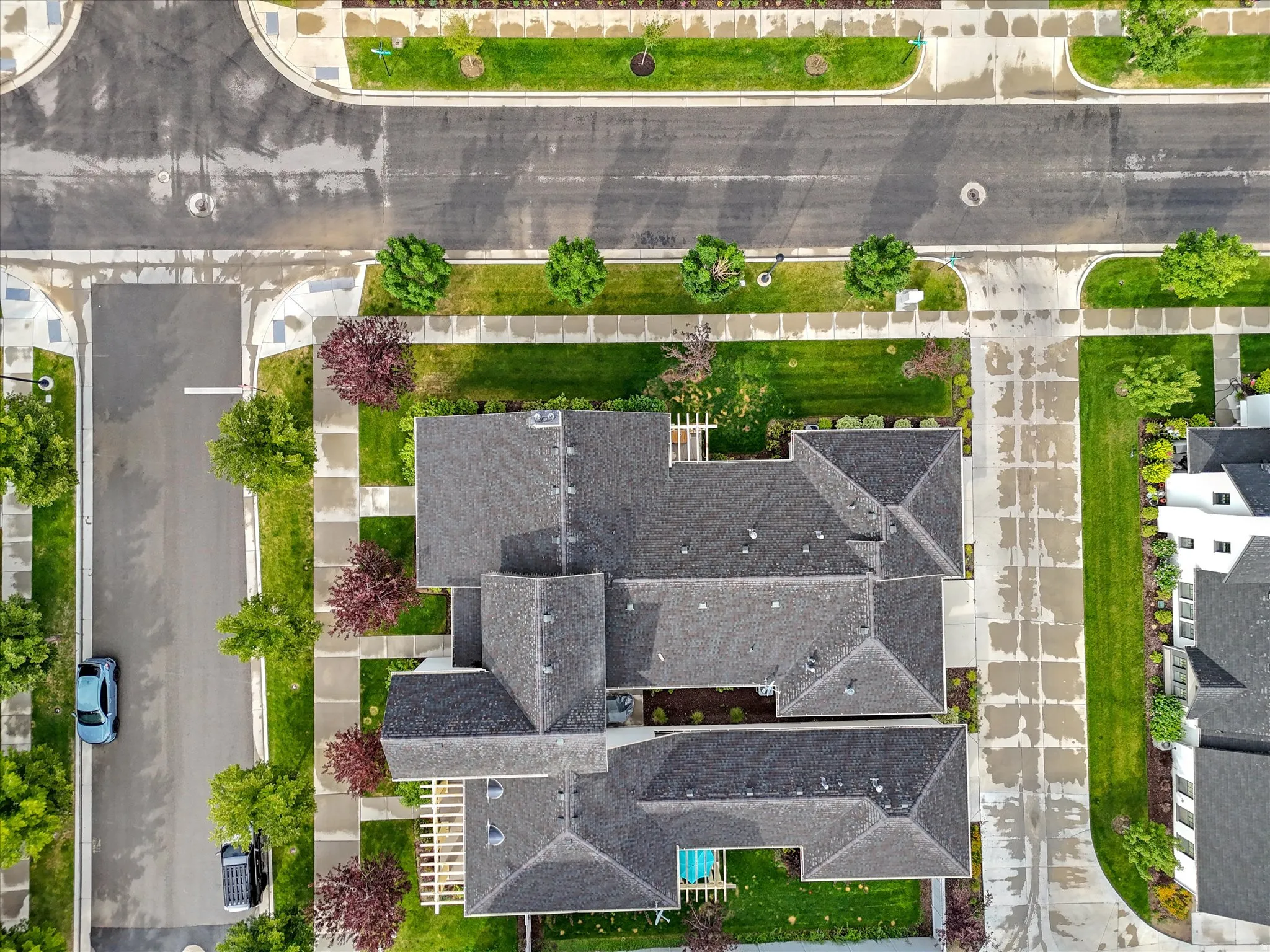 Property featuring an asphalt shingle roof, paved driveways, concrete sidewalks, and landscaped grounds with mature trees
