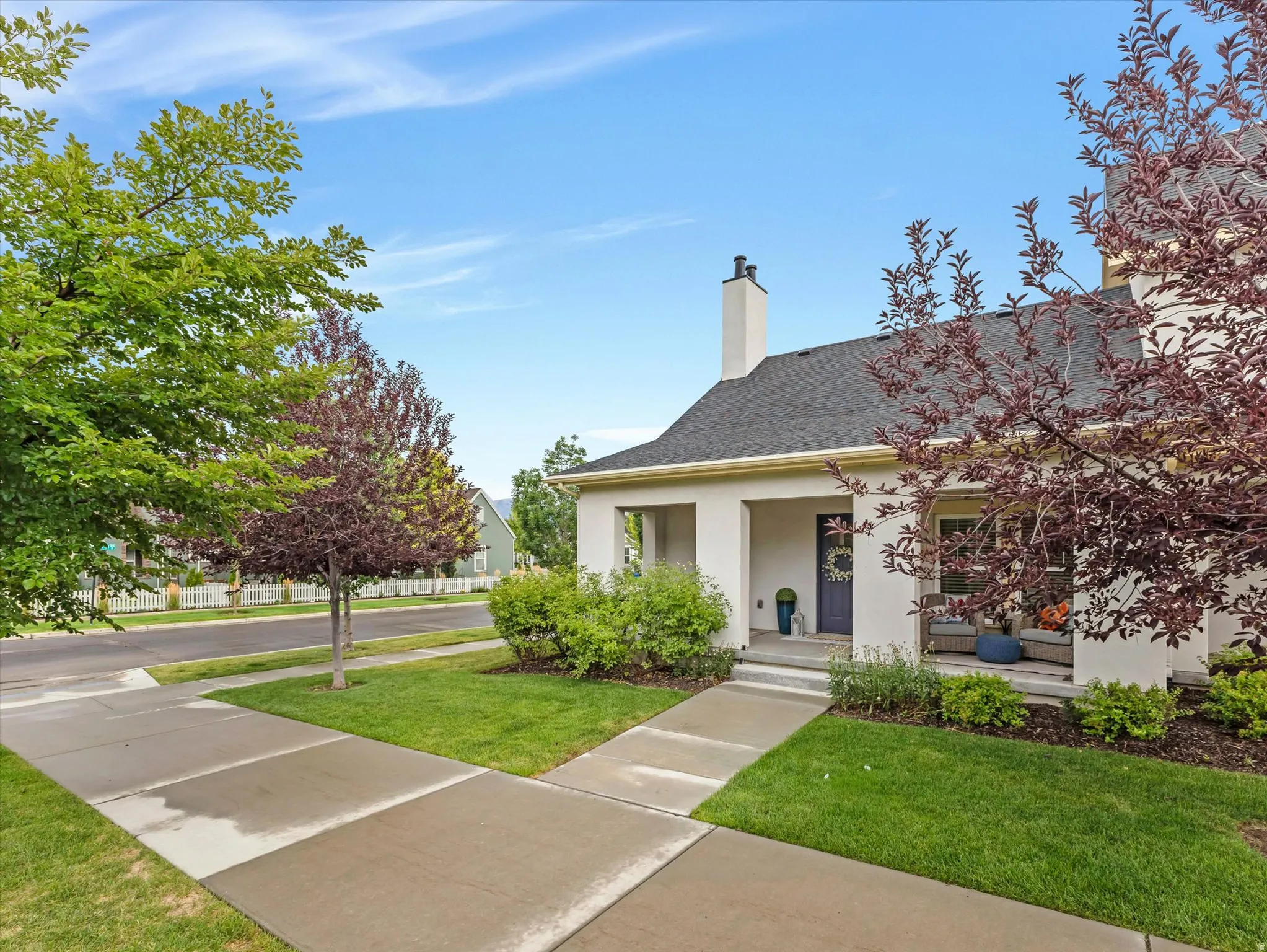 Stucco exterior with covered front porch, dark gray entry door, and dark shingle roof