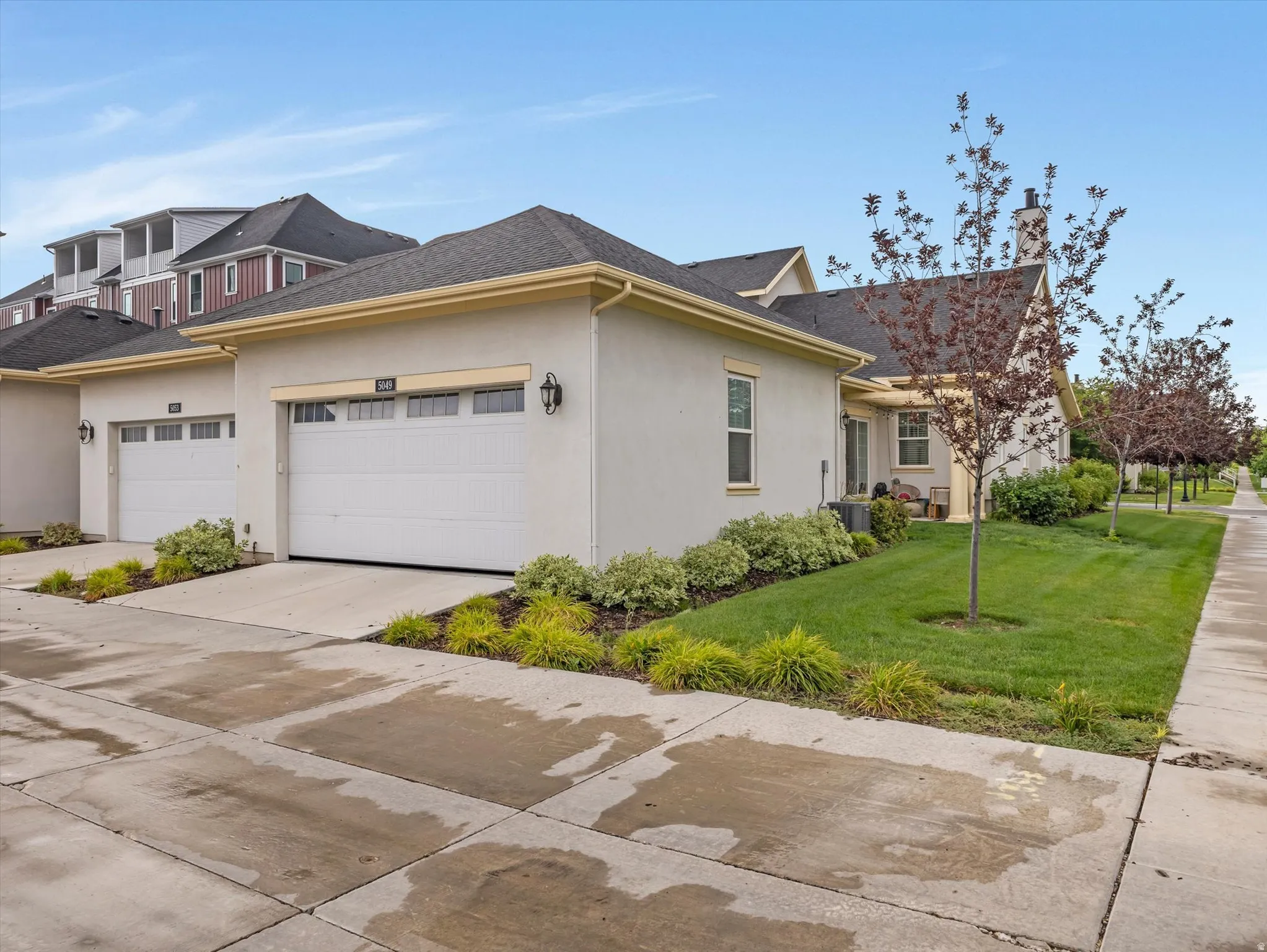 Stucco exterior with an attached garage, featuring a concrete driveway and sidewalk, and a manicured lawn with mature trees