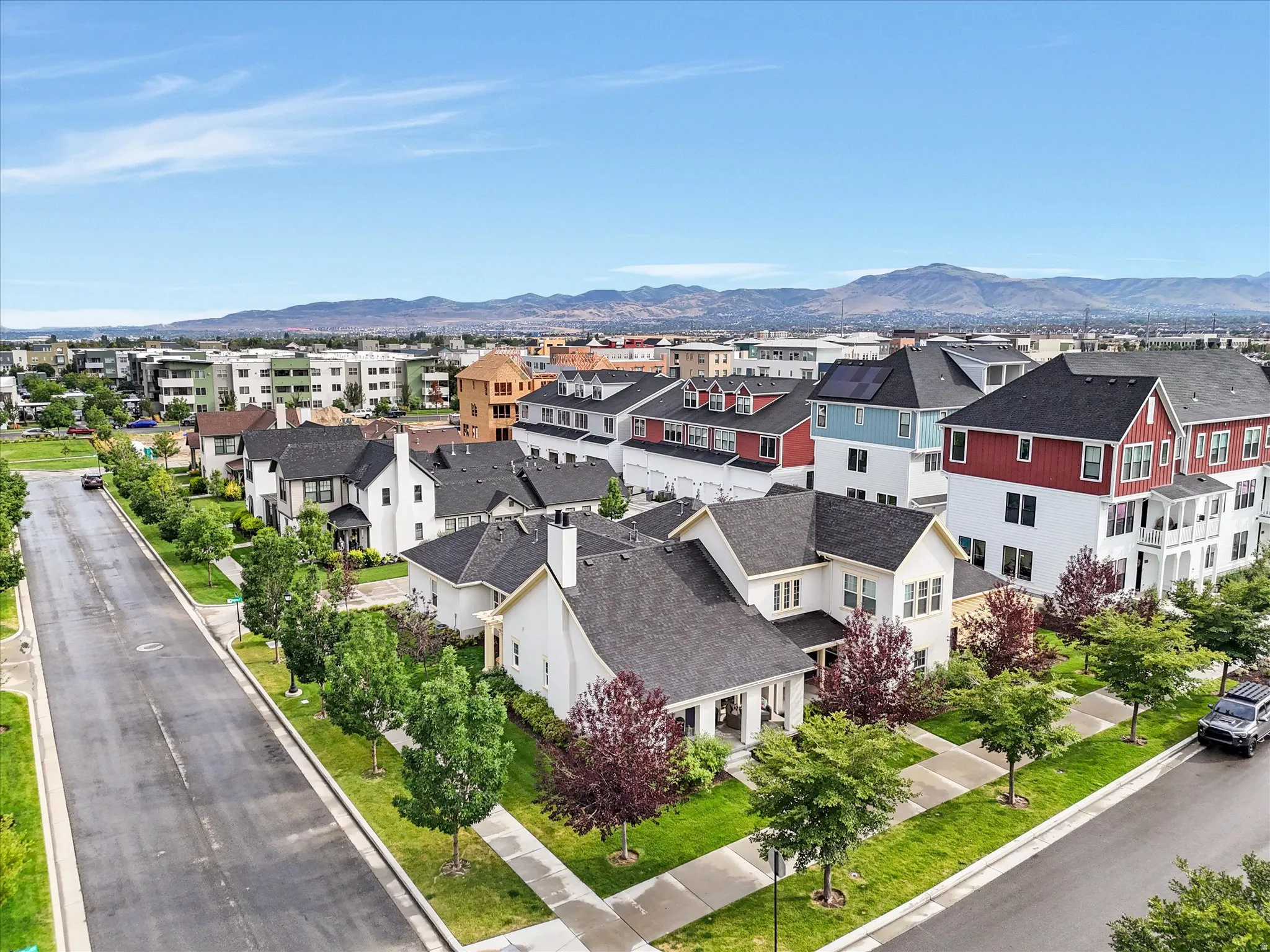 Residential neighborhood featuring a paved street, mature trees, manicured lawns, and mountains in the background
